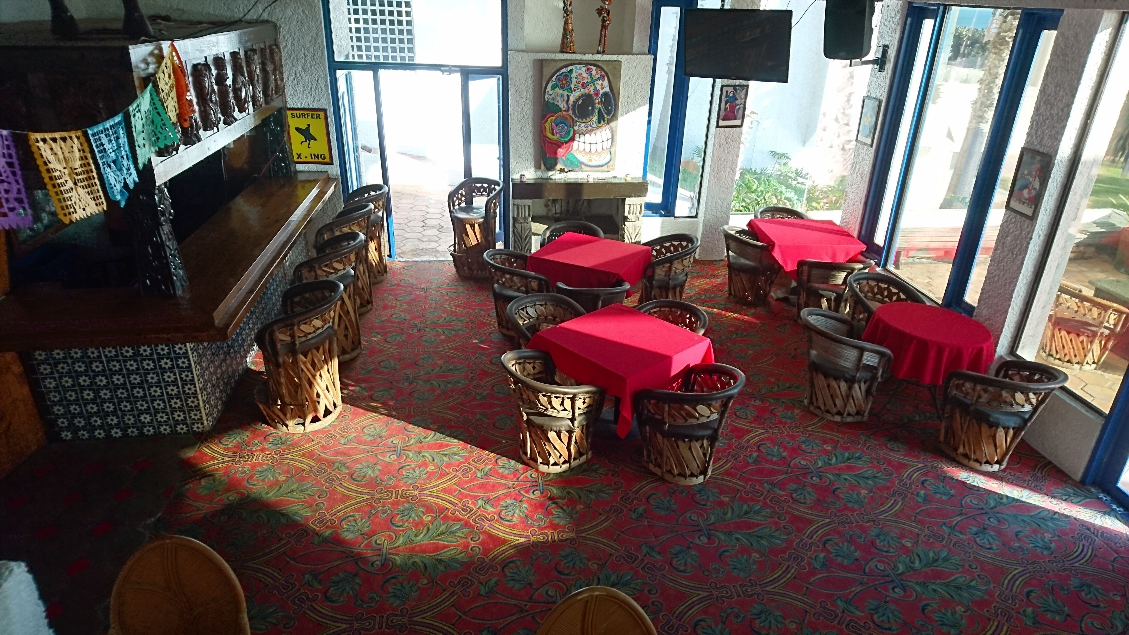A restaurant with red tablecloths, wicker chairs, and a patterned carpet.