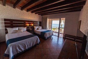 A hotel room with two beds, a wooden headboard, a nightstand, and a balcony with a view of the ocean.