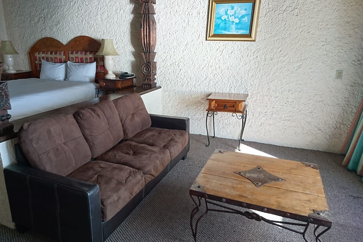 A room with a bed, a brown sofa, a wooden coffee table, and a small wooden side table.