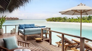 Une terrasse en bois avec un canapé, des chaises et une table sur laquelle se trouve un saladier. On aperçoit un grand parasol.