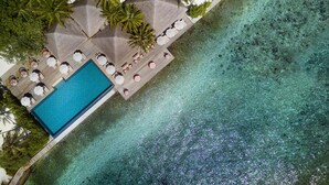 Vue aérienne d’un complexe hôtelier avec une piscine à l’eau cristalline, des chaises longues et des palmiers.