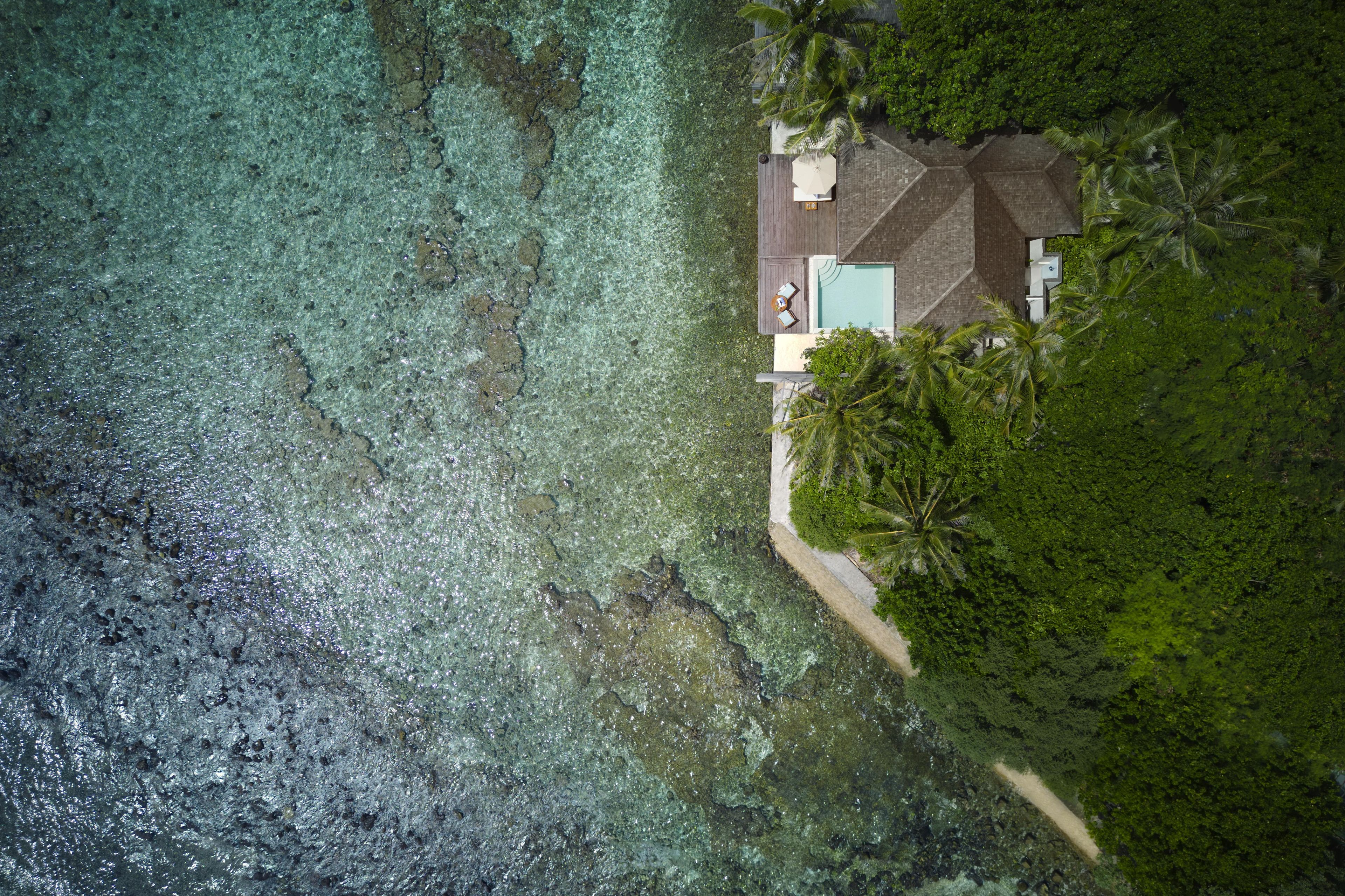 Vista aérea de uma casa com piscina, cercada por vegetação exuberante e água turquesa cristalina.