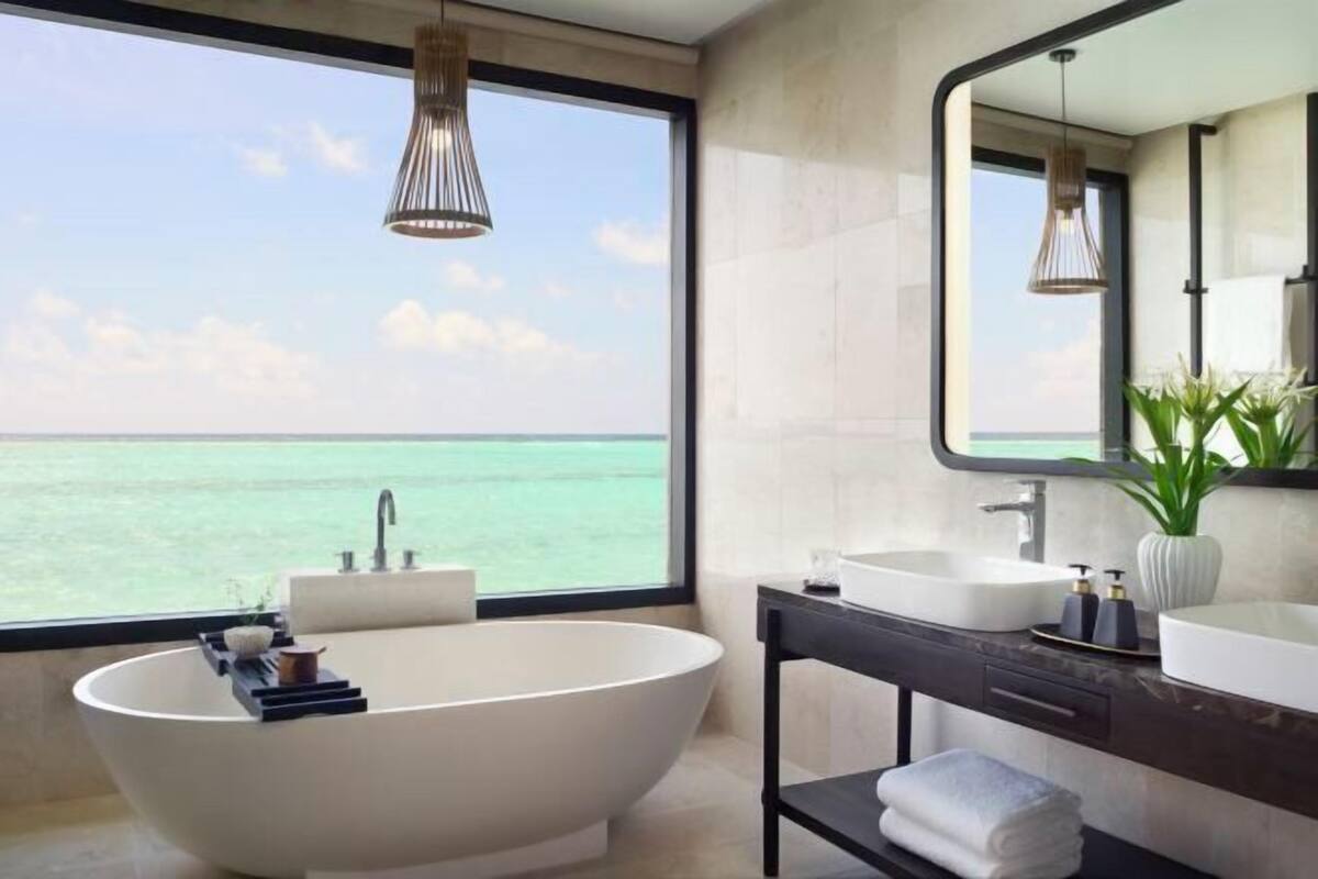 Une salle de bain moderne dotée d’une baignoire îlot, de deux vasques, d’un meuble-lavabo et d’une grande fenêtre offrant une vue sur la mer.