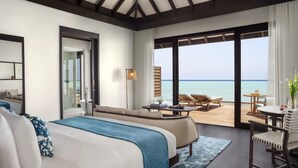 Une chambre d’hôtel moderne avec un grand lit, un canapé, une petite table et une vue sur l’océan.