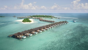 Un complexe hôtelier proposant des bungalows sur pilotis, avec différents types d’hébergements s’étendant au-dessus de la mer turquoise et reliés par des passerelles.