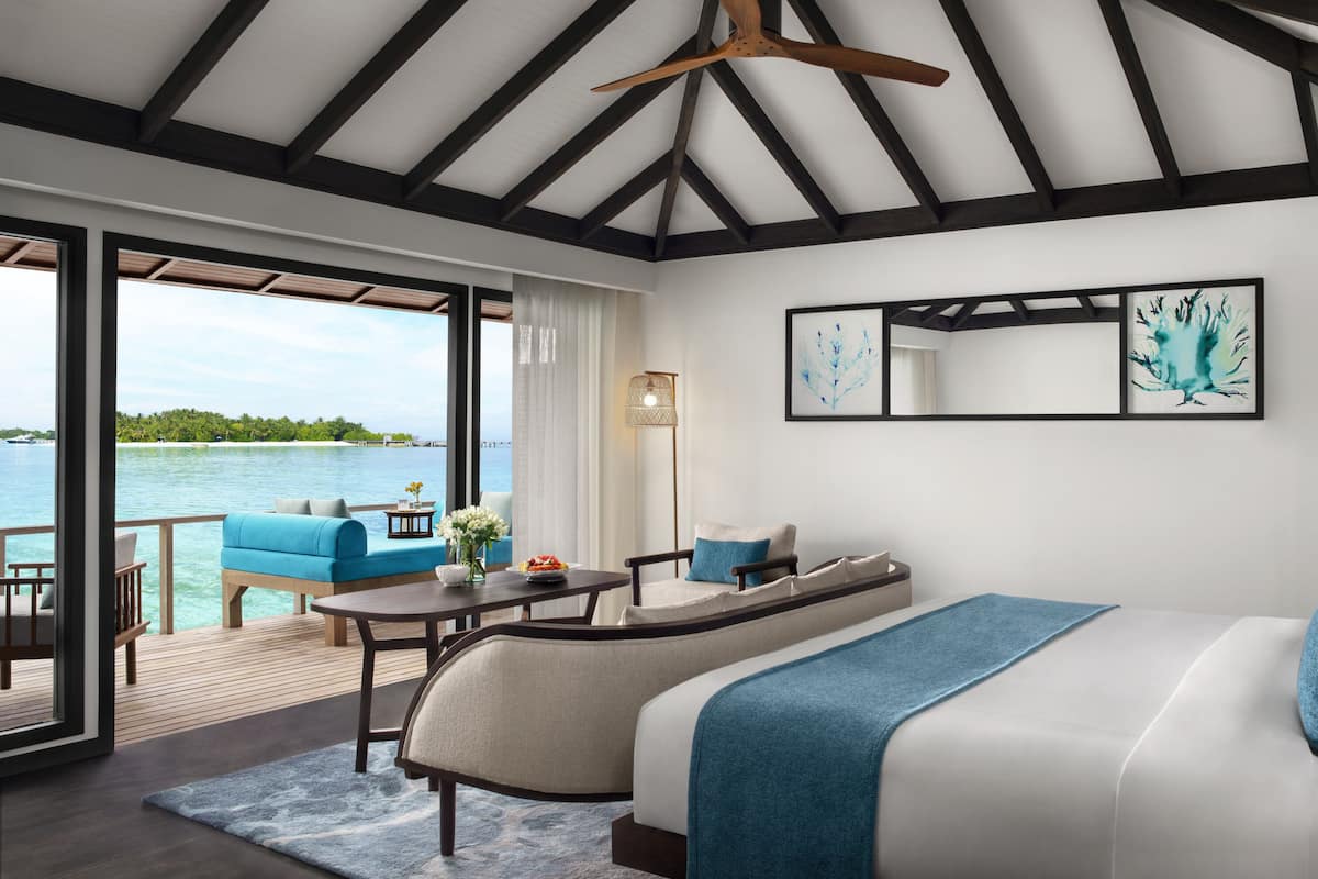 Een moderne slaapkamer met een groot bed, een bank en een eettafel. Er is uitzicht op zee en een terras buiten.