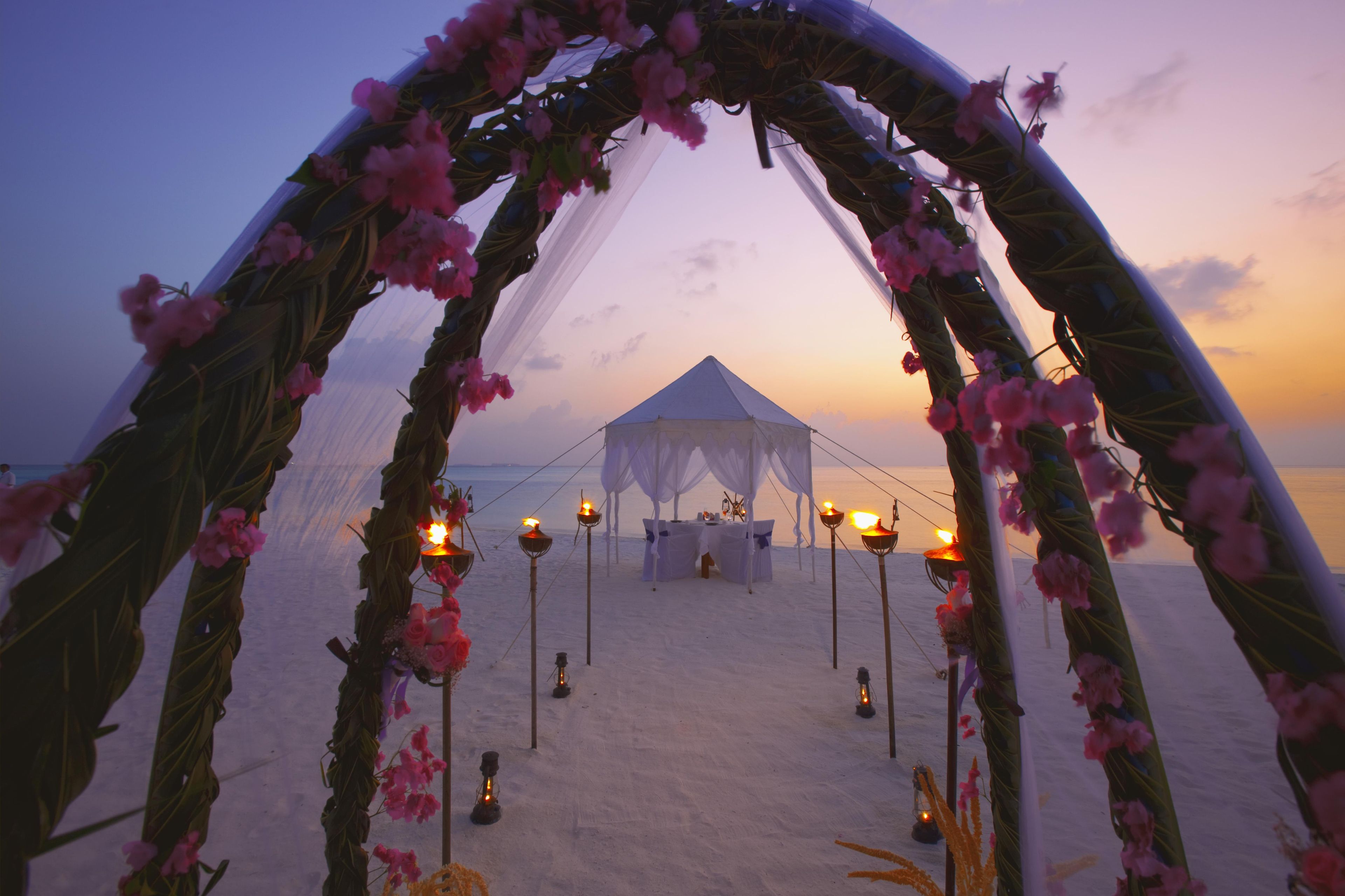 A beach wedding setup with a tent and floral arch.