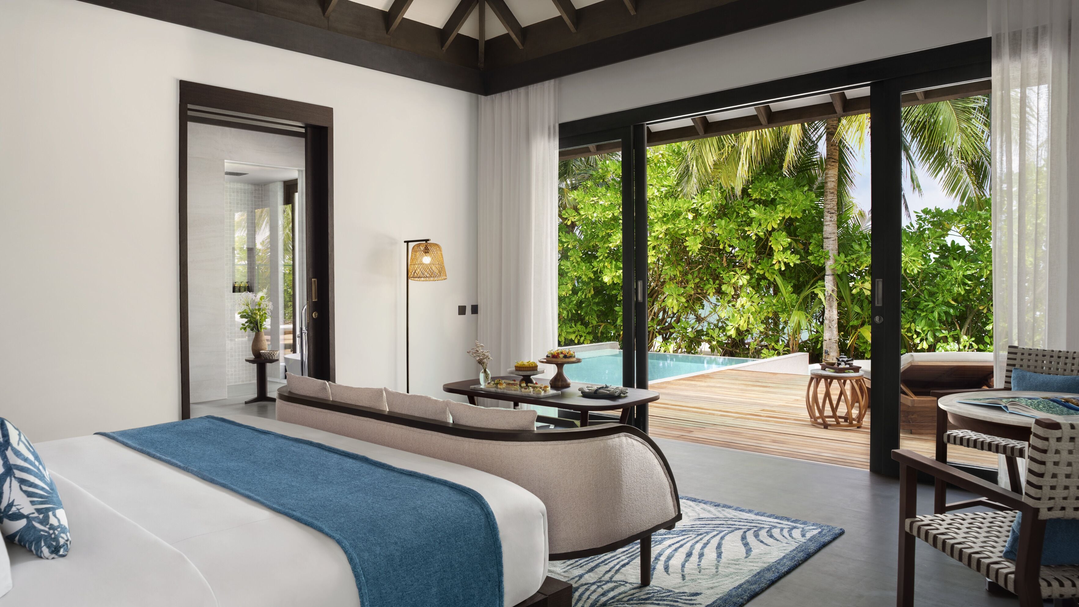 Un dormitorio moderno con una cama grande, una mesita con un florero y vistas a una piscina y vegetación.