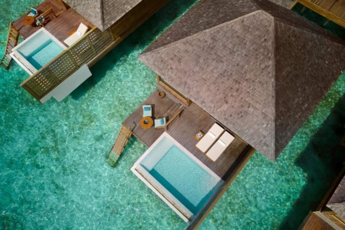Een luchtbeeld van bungalows op palen met zwembaden, houten dekken en lounge stoelen.