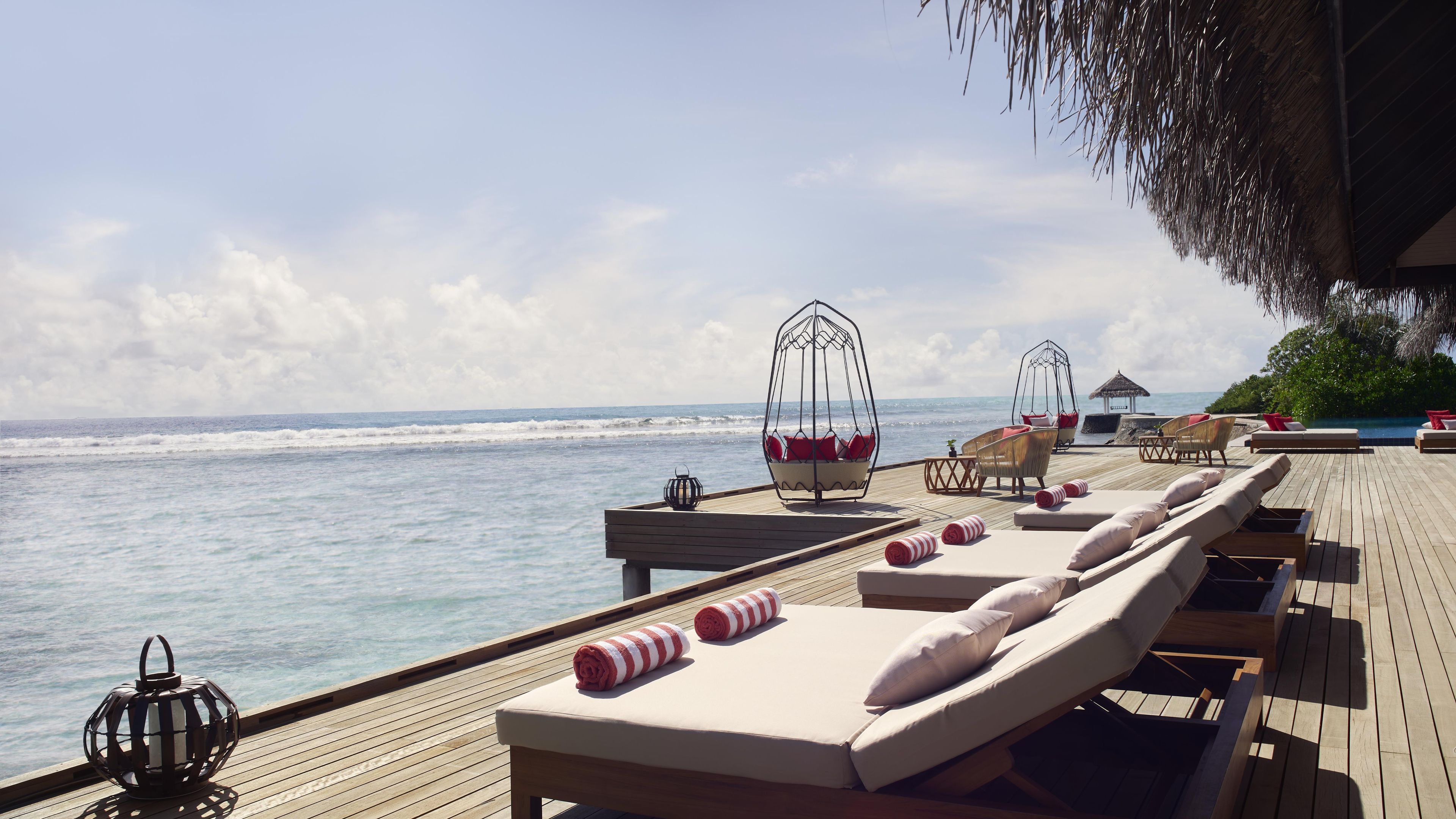 An outdoor deck with lounge chairs, a hanging chair, and a small table with a lantern.