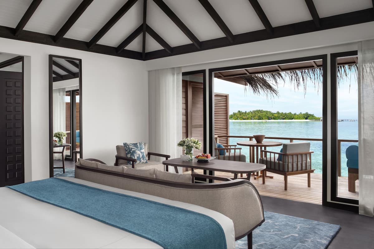 Een slaapkamer met een groot bed, een zithoek met een tafel en stoelen, en een balkon met uitzicht op het water.
