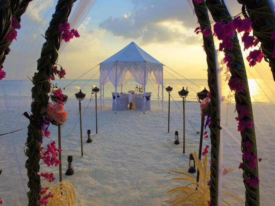 A wedding arch with pink flowers and a tent in the background.