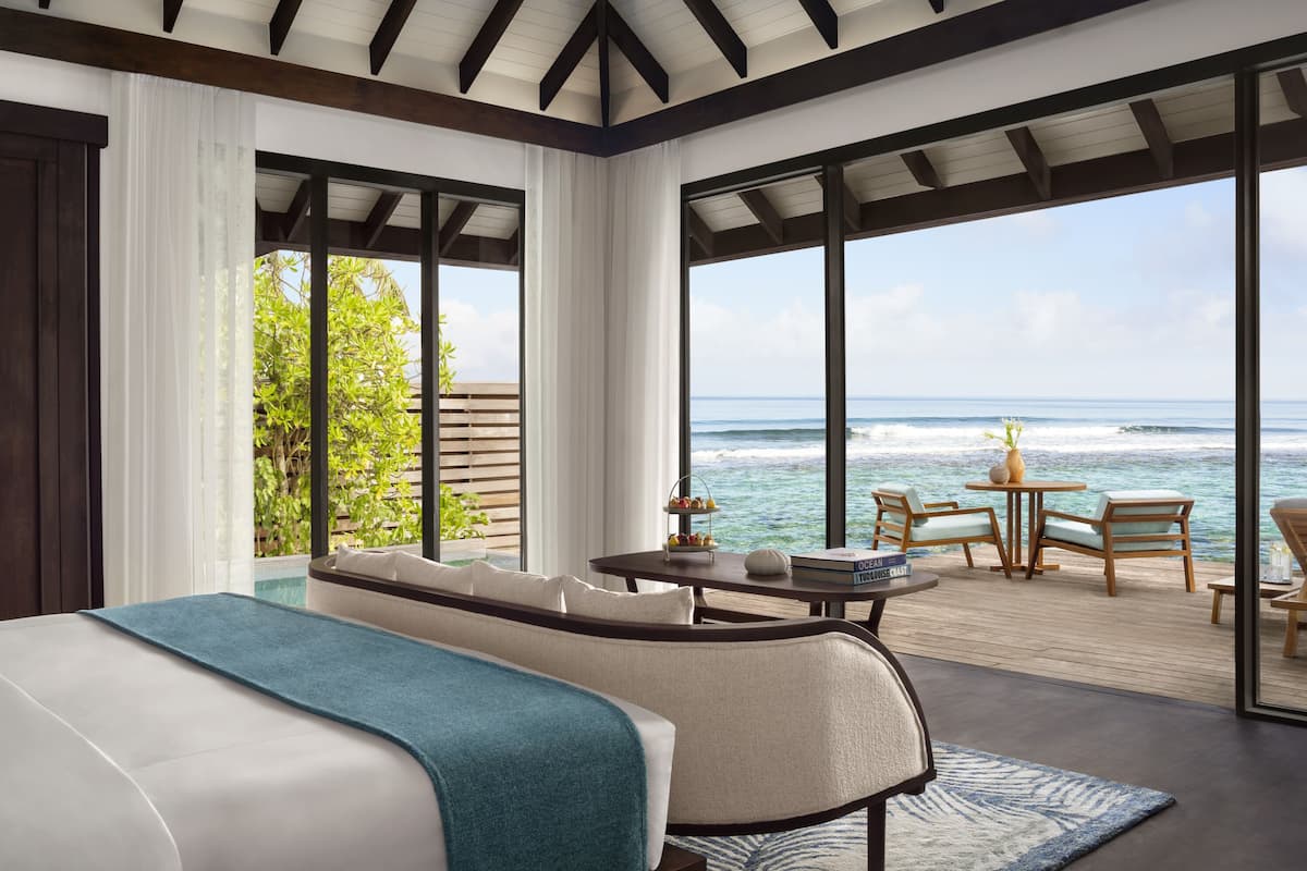 Een slaapkamer met een groot bed, een sofa, een tafeltje met boeken en uitzicht op de oceaan.