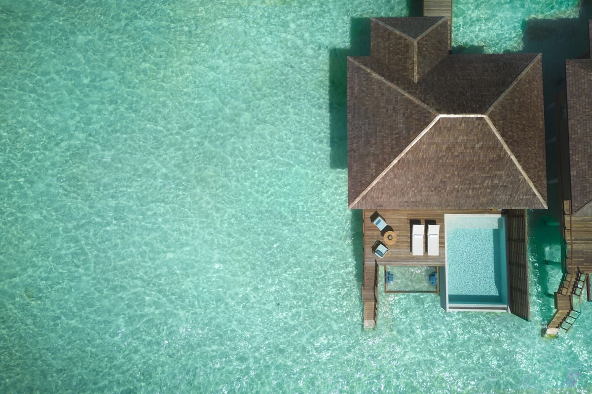 Een overwaterbungalow met een zwembad, een loungegedeelte en een houten terras.