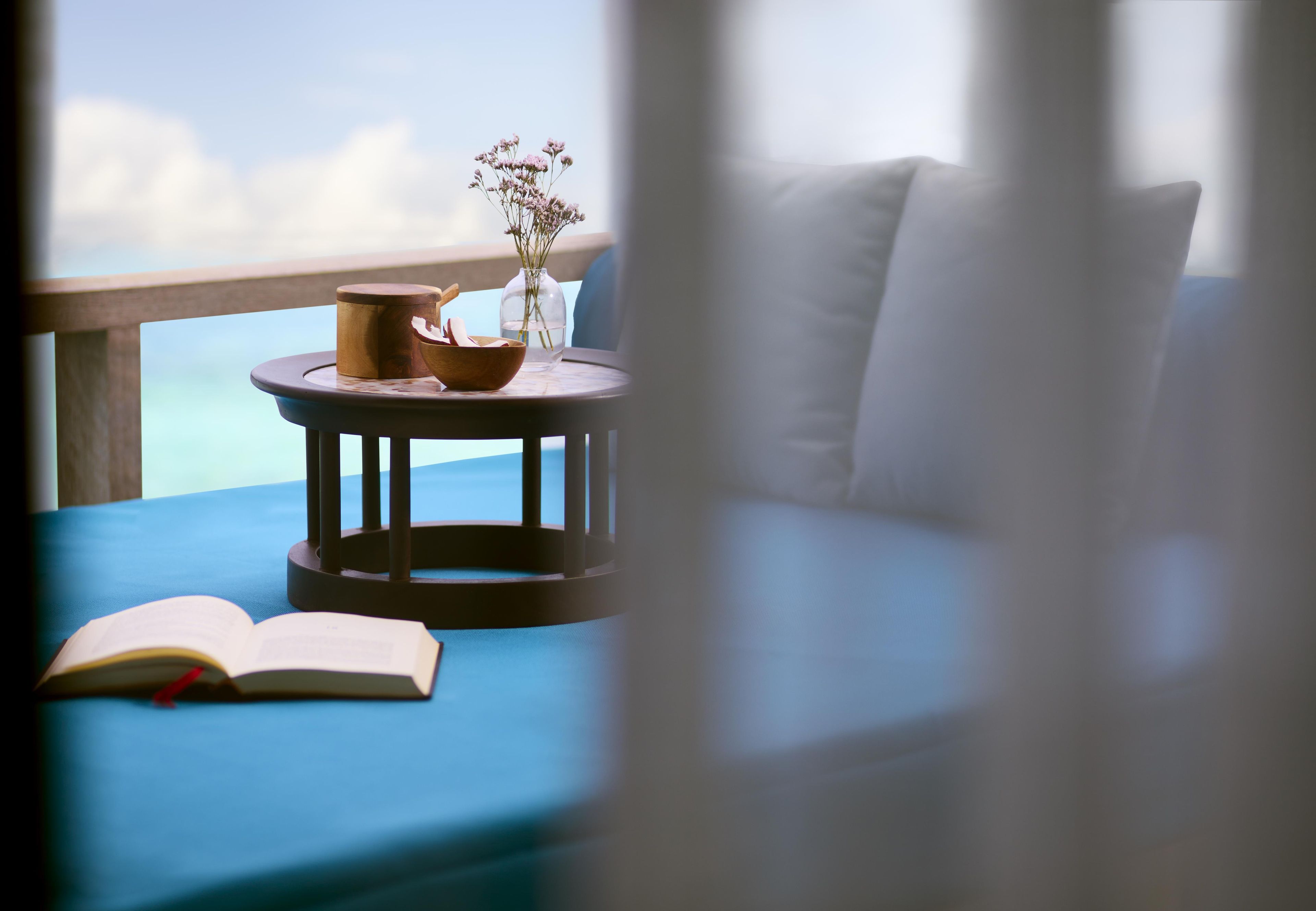 A balcony with a round table, a book, and a vase with flowers.