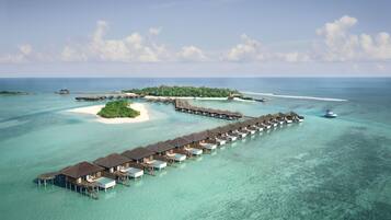 An overwater bungalows resort with a long pier extending into turquoise waters, surrounded by lush greenery and clear skies.