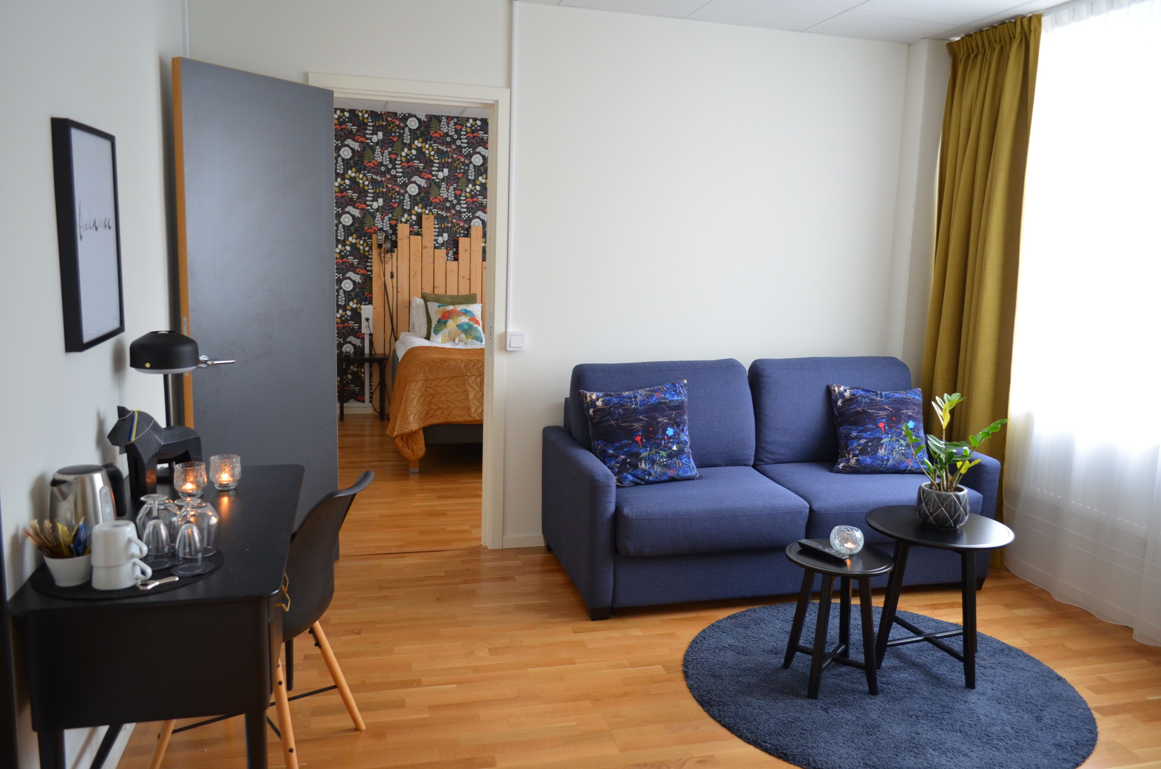 Een moderne woonkamer met een blauwe bank, een klein bijzettafeltje en een bureau met een lamp.