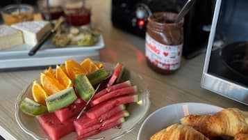 A breakfast table with fruit, croissants, and a jar of jam.
