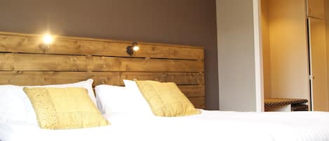 A neatly made bed with white linens and two decorative pillows, a wooden headboard, and a wall-mounted light fixture.