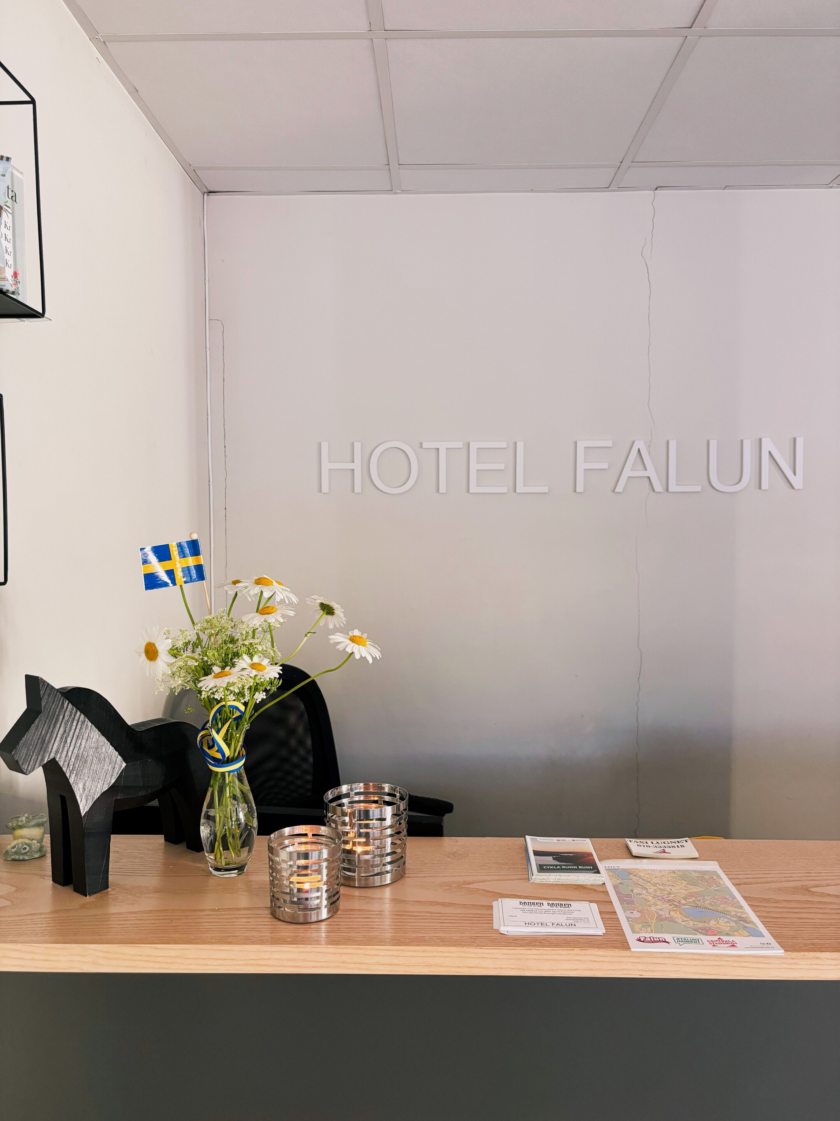A reception desk with a vase of flowers, a Swedish flag, and a map of Falun.