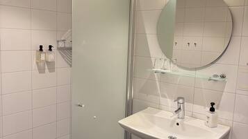 Et moderne badeværelse med en glasbrusekabine, en hvid vask med et rundt spejl og en glashylde over vasken.