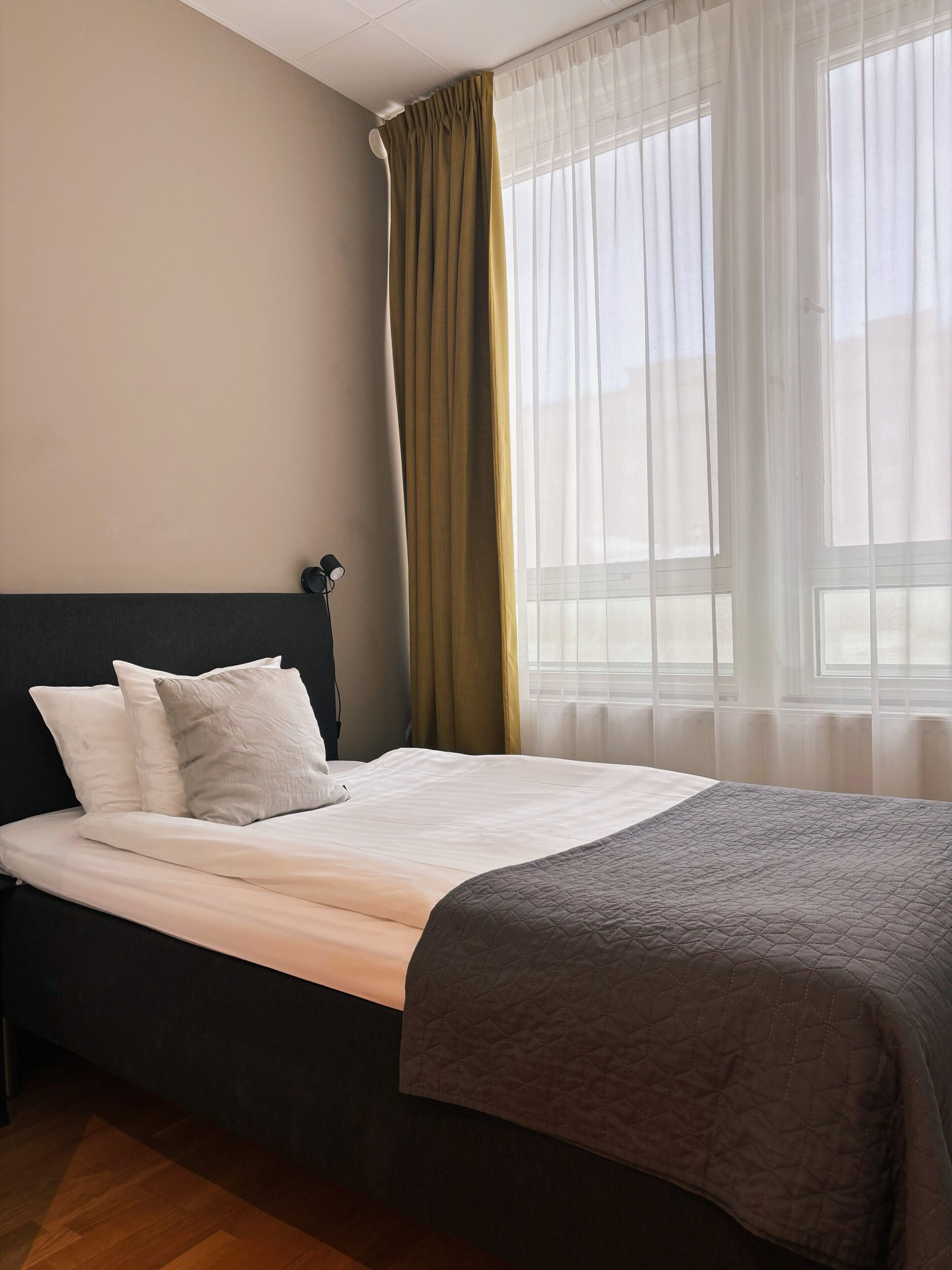 A neatly made bed with a dark headboard, a grey quilted blanket, and two pillows.