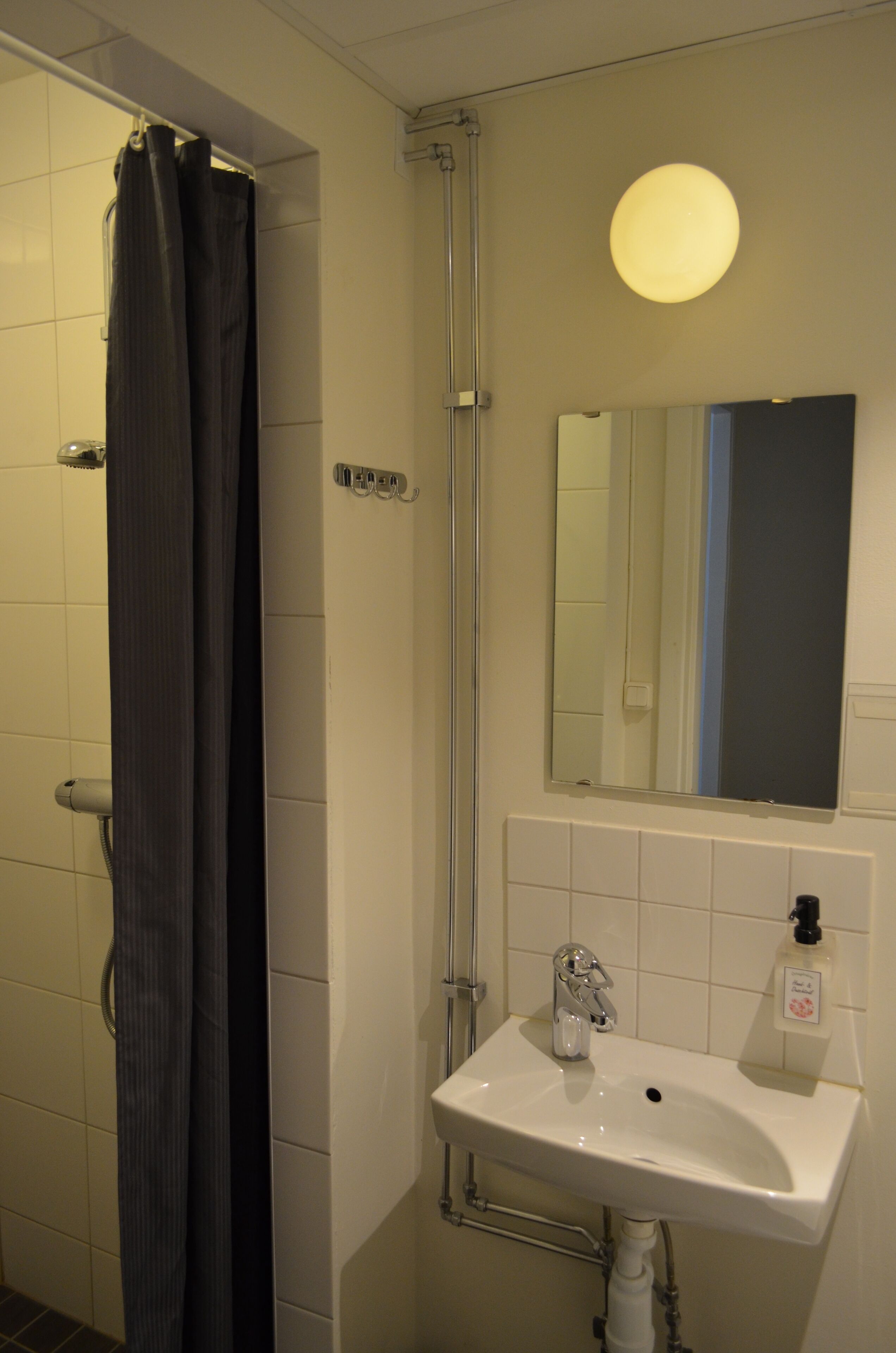 A bathroom with a shower, a sink, a mirror, and a light fixture.