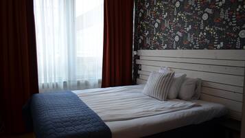 Una habitación de hotel con cama, ventana con cortinas traslúcidas, pared con diseño y cabecera de madera.
