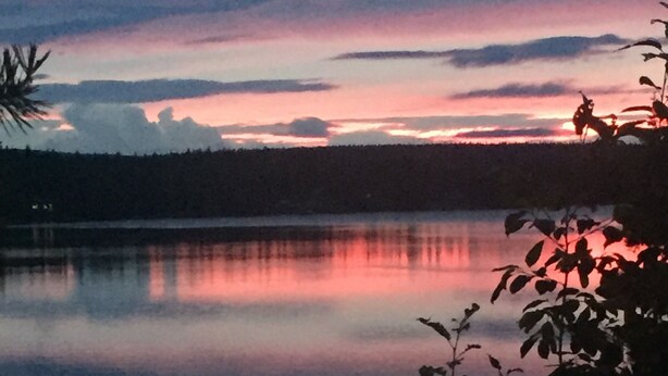 Un lago tranquilo al atardecer, con la silueta de una persona en un bote a lo lejos.
