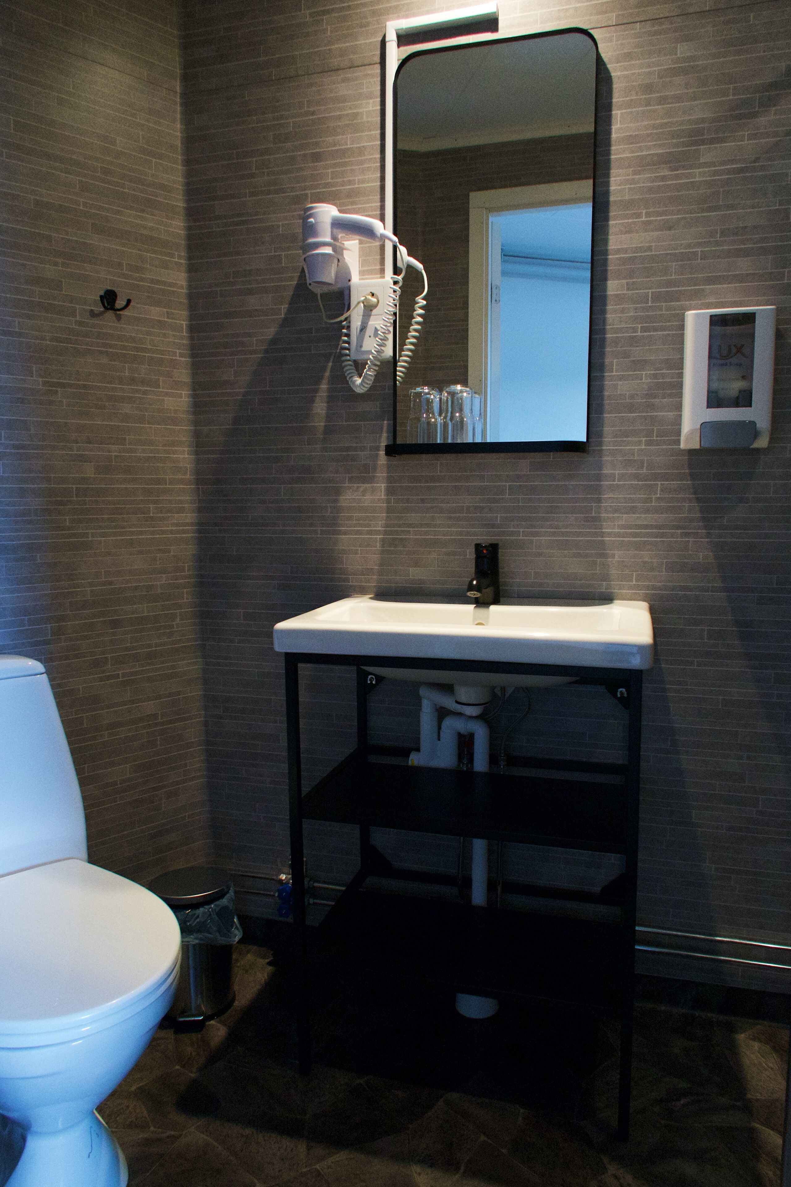 A bathroom with a white toilet, a sink with a mirror above it, and a hairdryer mounted on the wall.