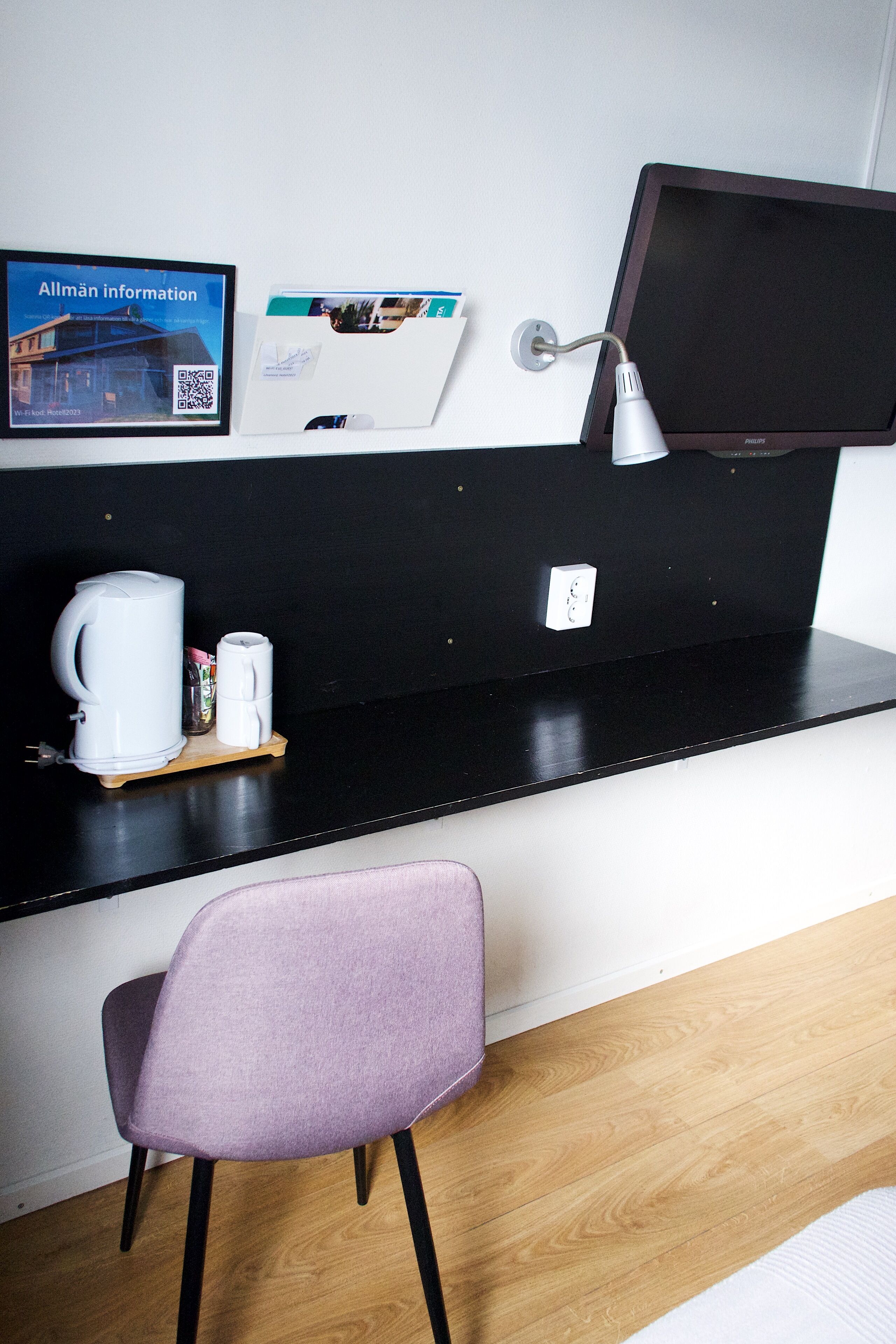 Ein Hotelzimmer mit schwarzem Tresen, einer weißen Kaffeemaschine, einem violetten Sessel und einem flachbildfernseher, der an der Wand montiert ist.