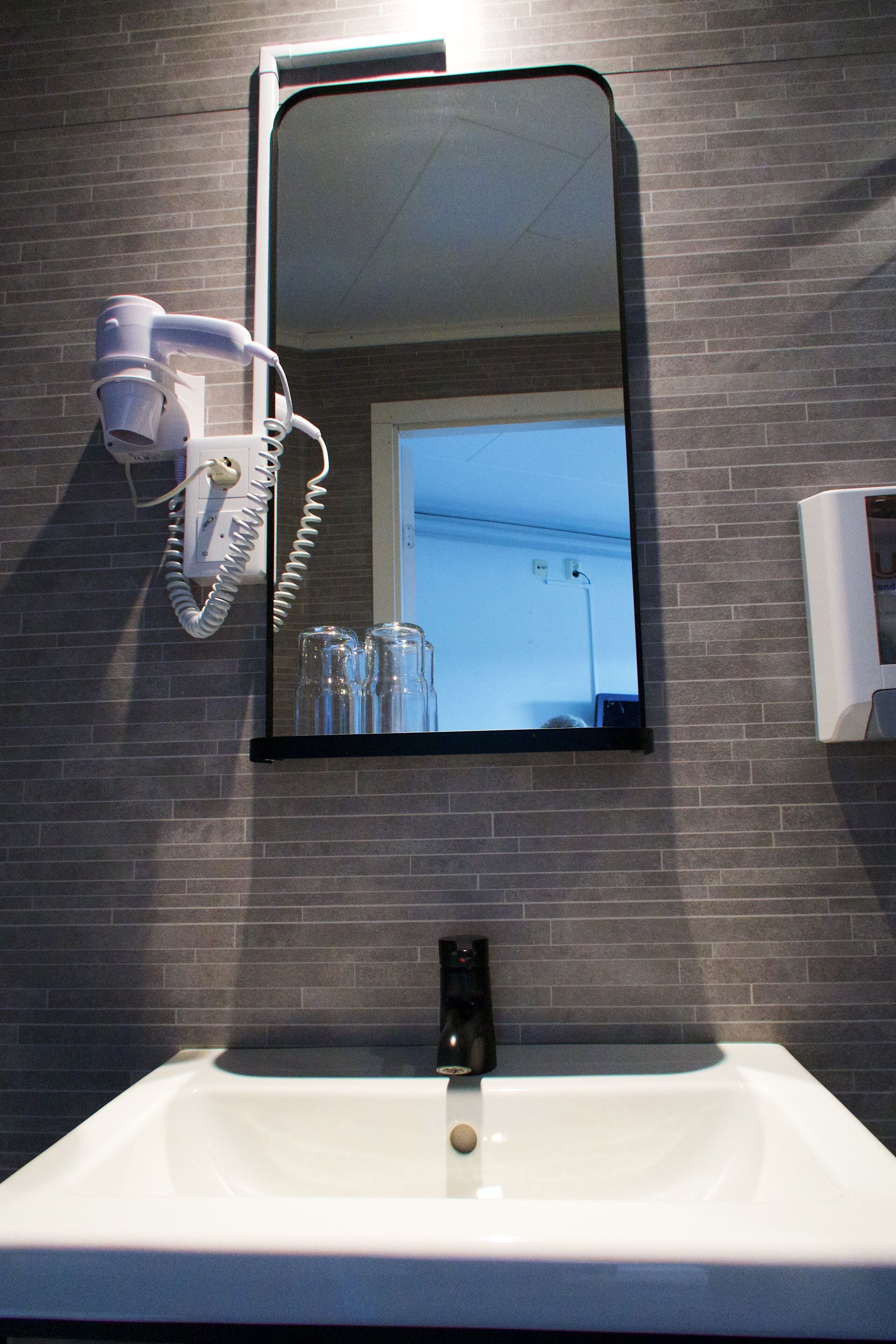 A bathroom with a white sink, a hairdryer mounted on the wall, and a mirror above the sink.