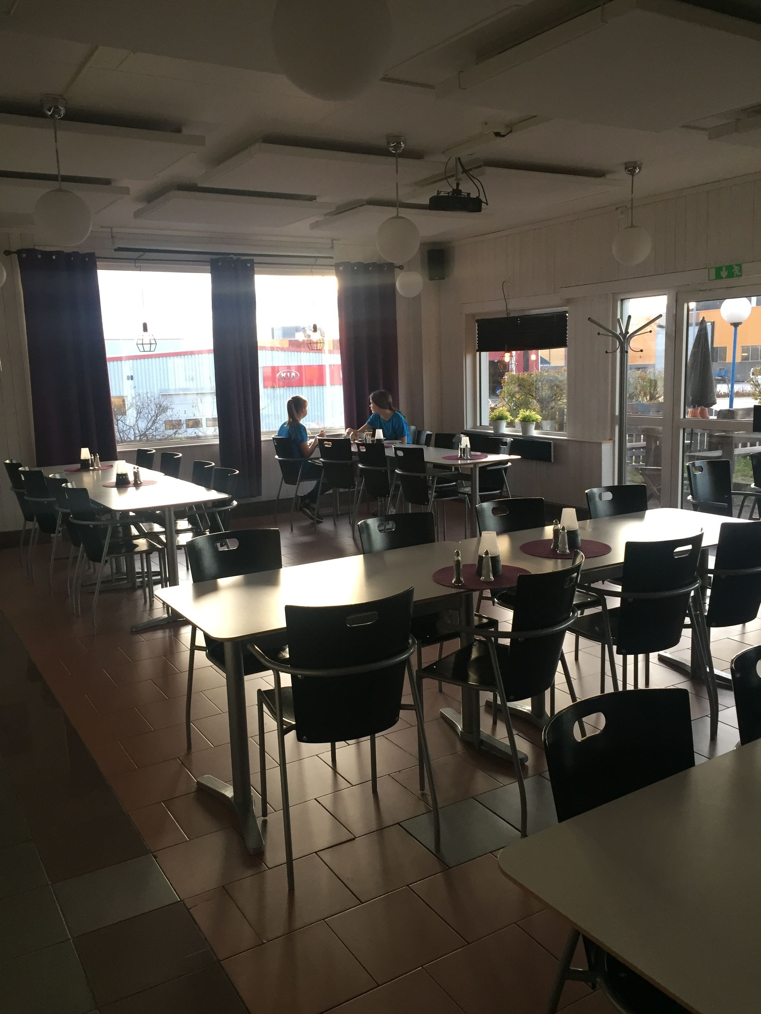 Un vaste espace dédié à la salle à manger, avec de nombreuses tables et chaises, de grandes fenêtres dotées de rideaux et une vue sur l’extérieur.