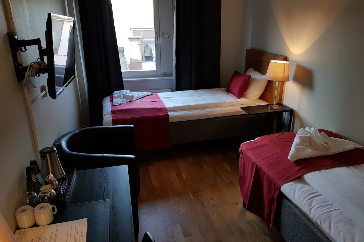 A hotel room with two beds, a desk with a chair, a lamp, and a view of the outside.
