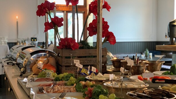 A buffet with various food items, including meats, cheeses, and fruits, arranged on a counter with serving utensils.