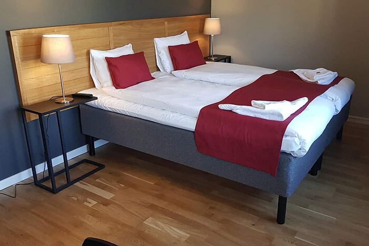 A double bed with white and red bedding, two bedside tables with lamps, and a wooden headboard.