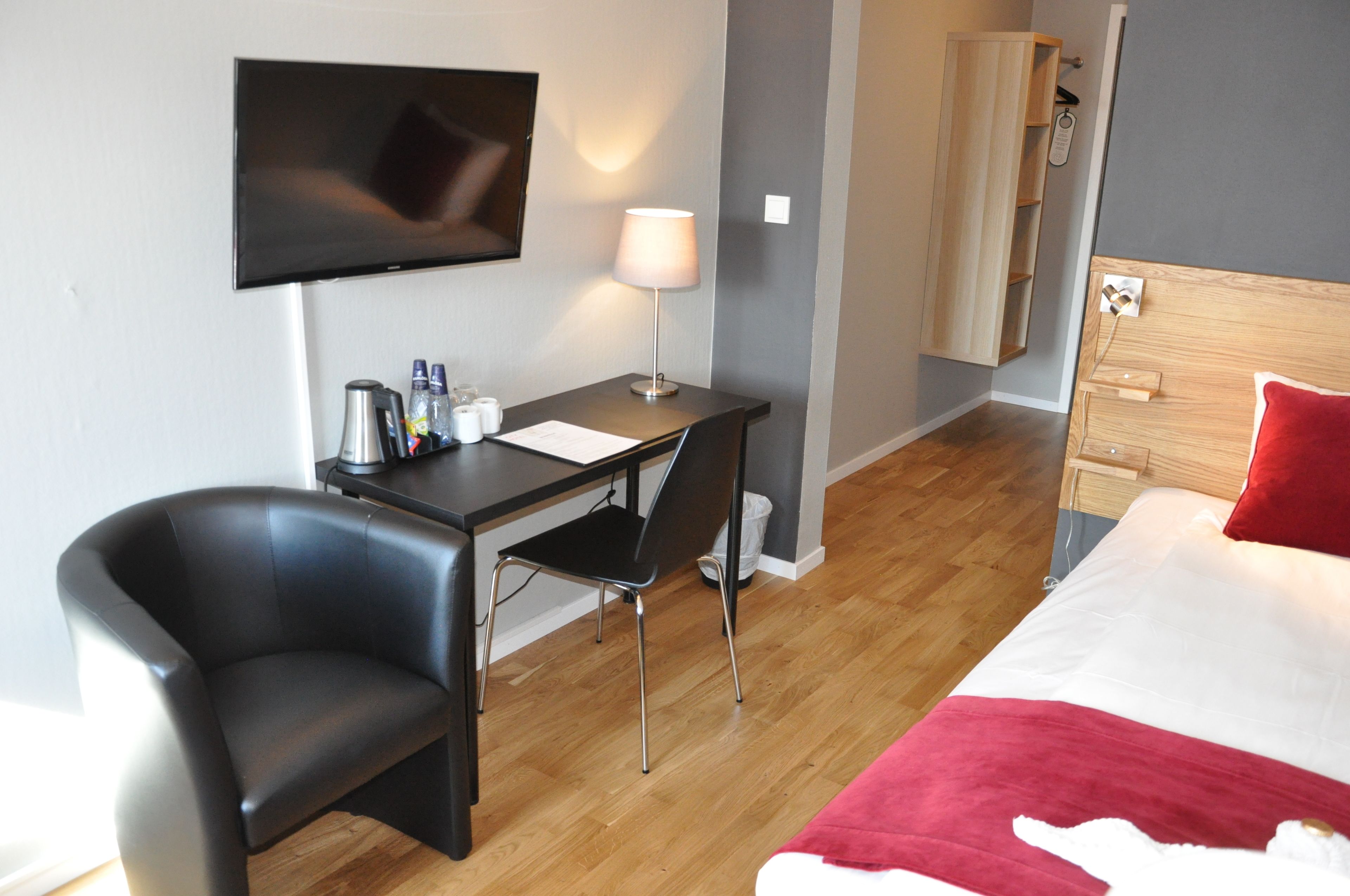 Ein Hotelzimmer mit Bett, Schreibtisch, Stuhl, Fernseher, Lampe und Kleiderschrank.