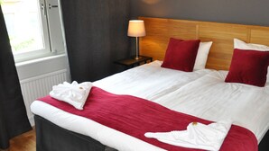 A neatly made bed with white and red bedding, a bedside table with a lamp, and a window with curtains.