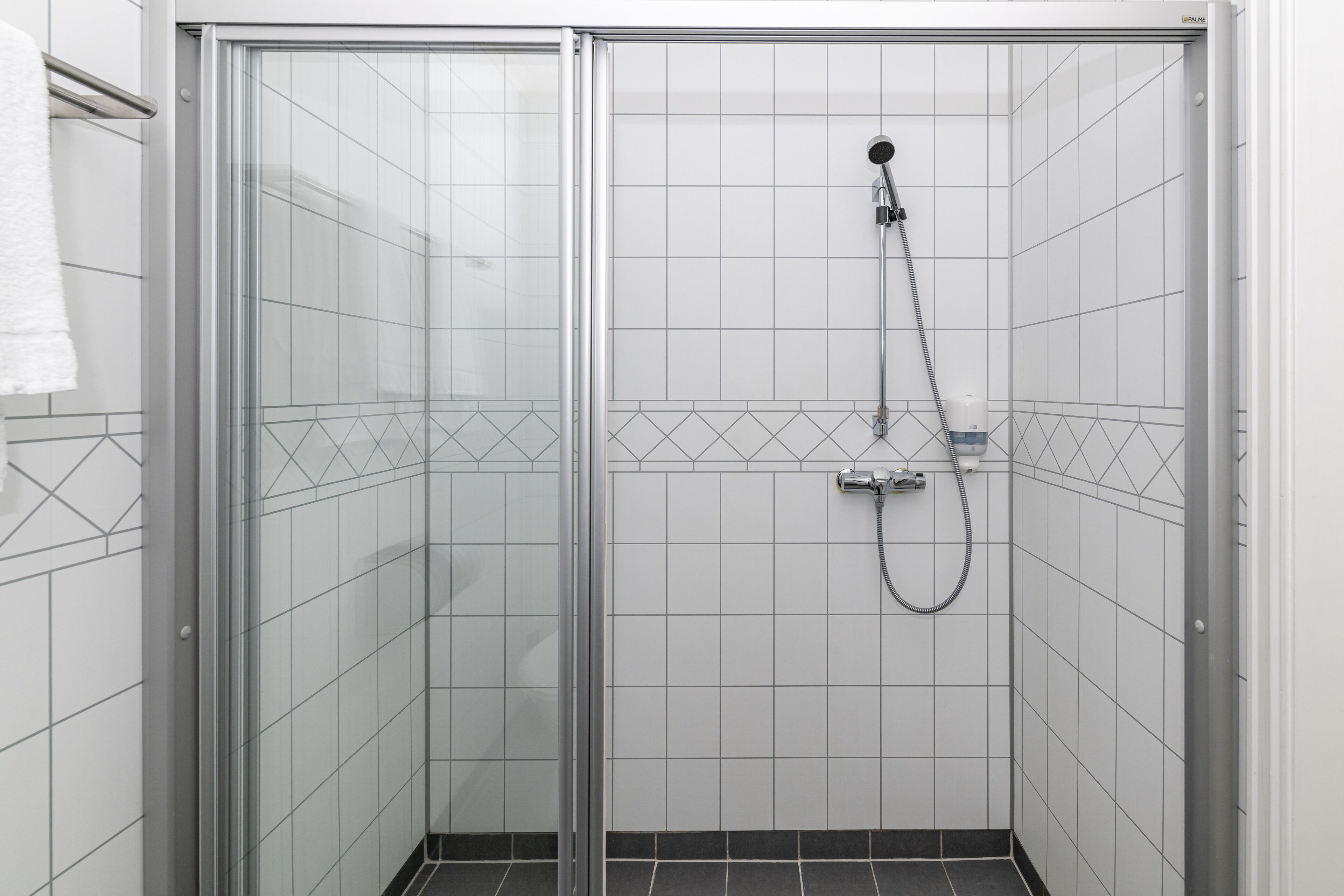 Een douchecabine met glazen wanden, een handdouche en een wandmengkraan.