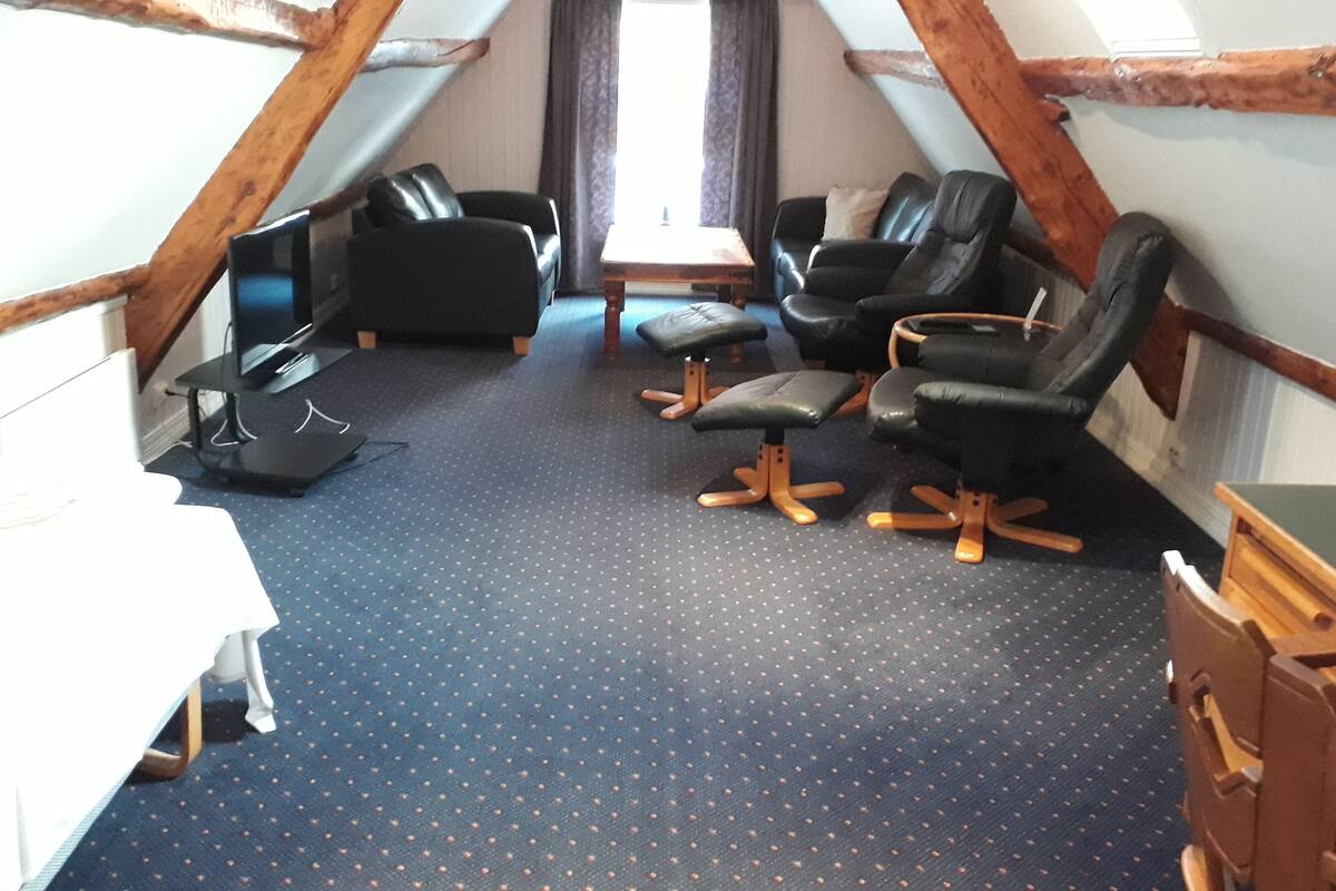 A small, cozy room with a blue carpet, a desk, two black chairs, and a small table.