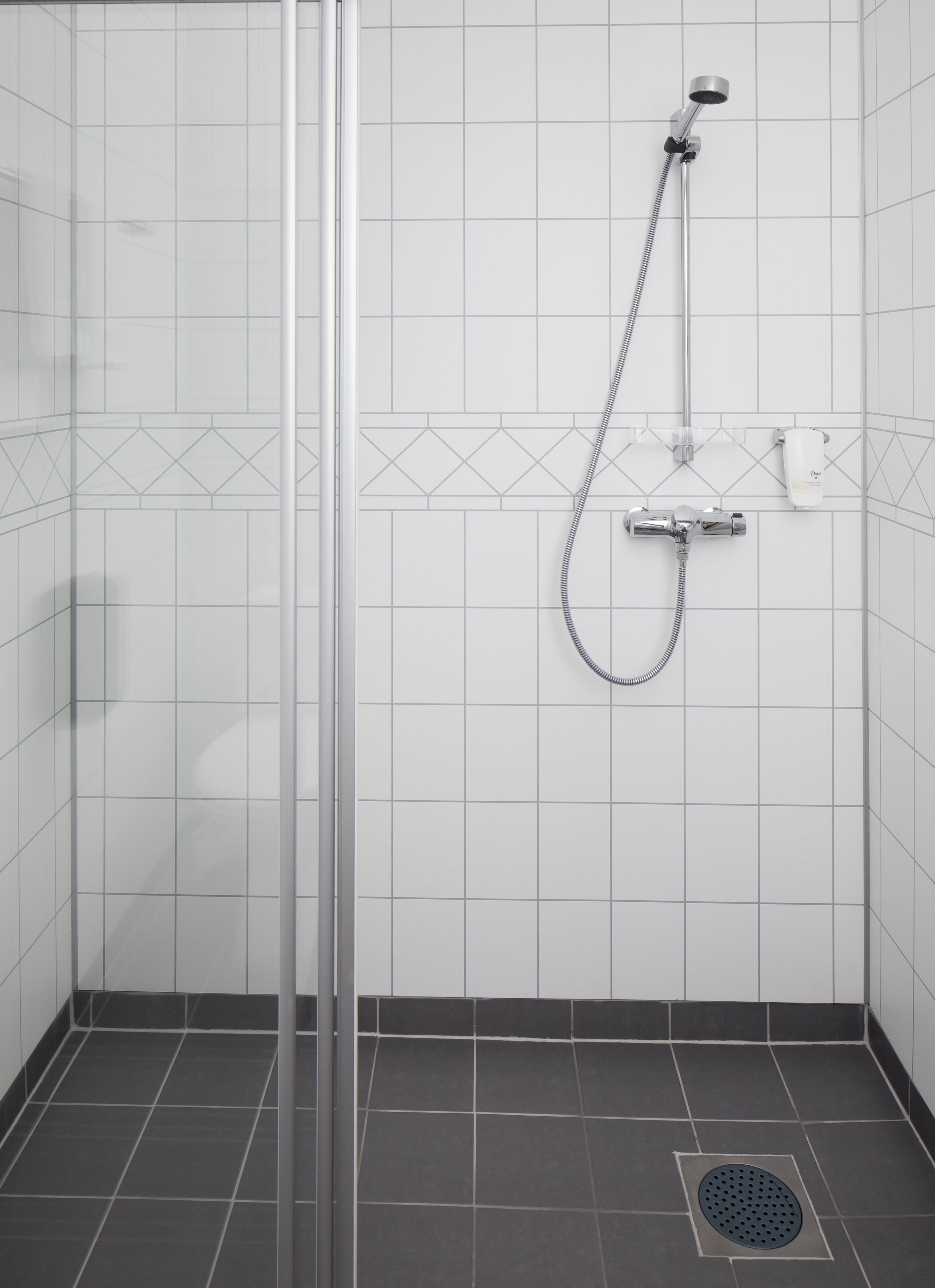 A shower area with a glass door, white tiled walls, and a showerhead mounted on the wall.
