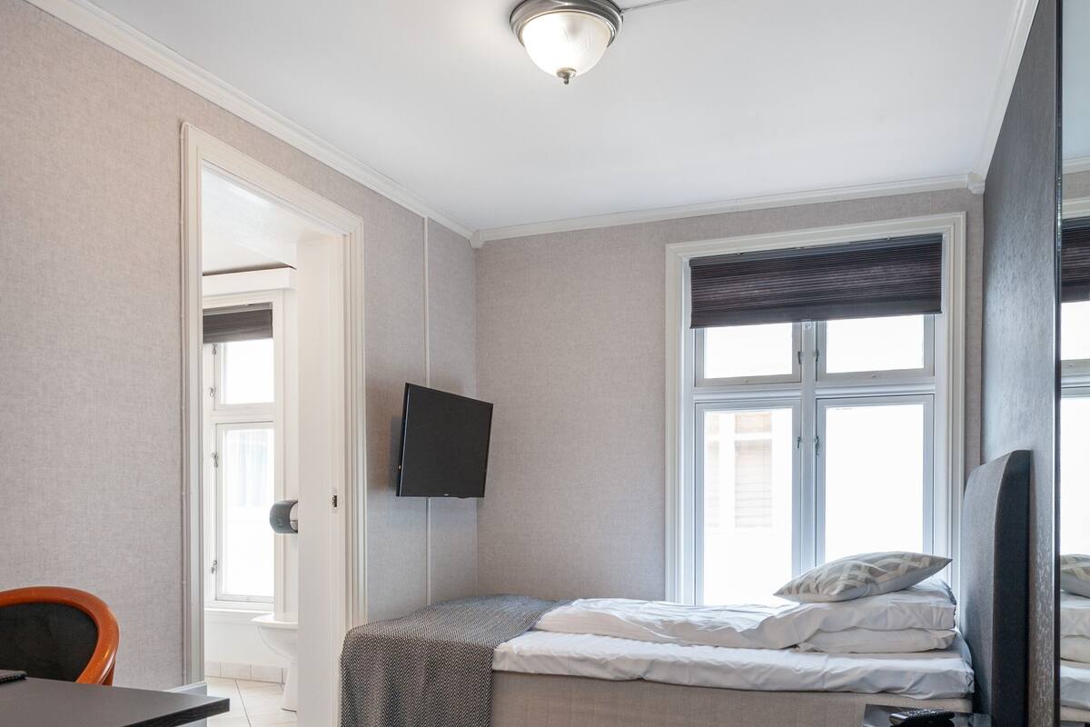 A small, modern bedroom with a bed, a desk, and a TV.