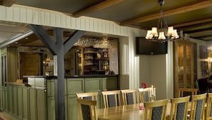 A dining area with a wooden table and chairs, a patterned rug, and a bar area with shelves of bottles and glasses. - Kjøbmandsgaarden Hotel (Lindesnes)