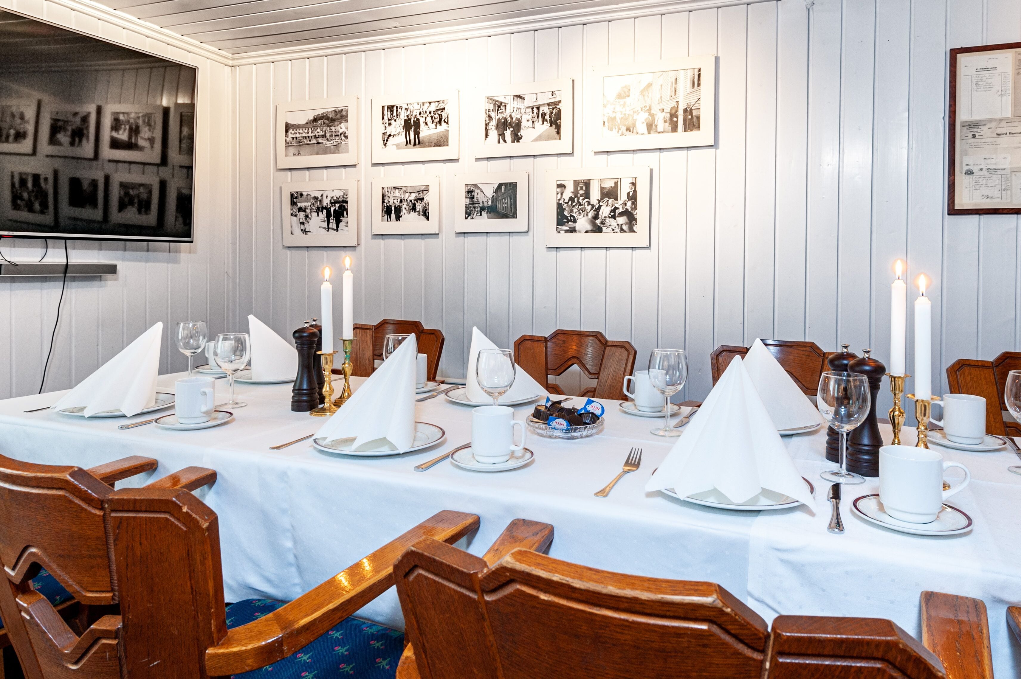 A dining table set with white tablecloths, candles, and wooden chairs.