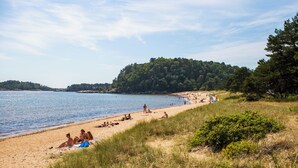 A beach with people sunbathing and swimming, surrounded by trees and hills. - Kjøbmandsgaarden Hotel (Lindesnes)