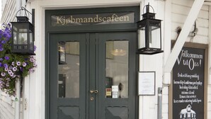 A building entrance with a dark green door labeled "Kjøbmandscaféen". - Kjøbmandsgaarden Hotel (Lindesnes)