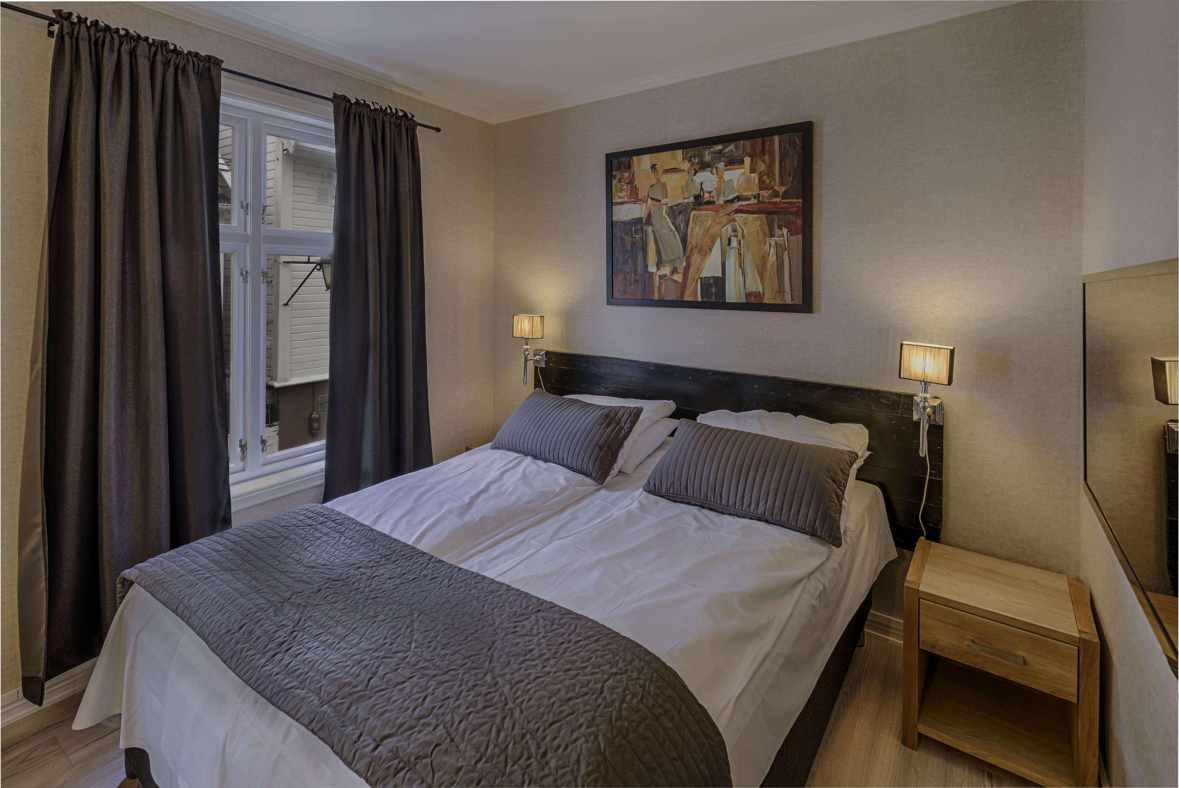 Habitación de hotel con una cama grande, dos lámparas de noche, un cuadro en la pared y una mesita de noche de madera.