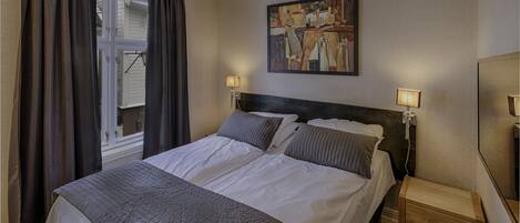 A hotel room with a large bed, two bedside lamps, a painting on the wall, and a wooden nightstand.