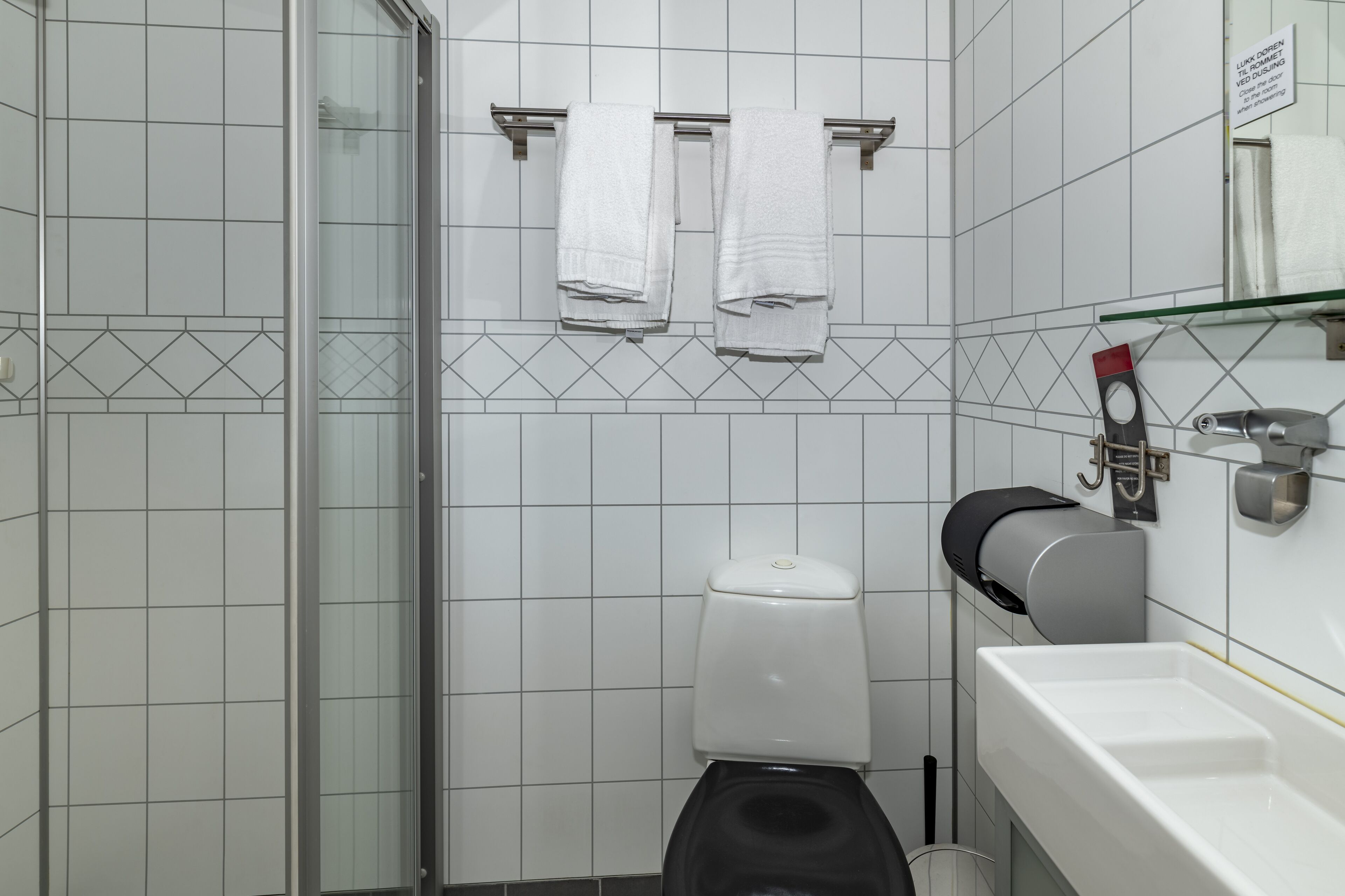 A modern bathroom with a glass shower enclosure, a toilet with a paper towel dispenser, and a sink with a soap dispenser.