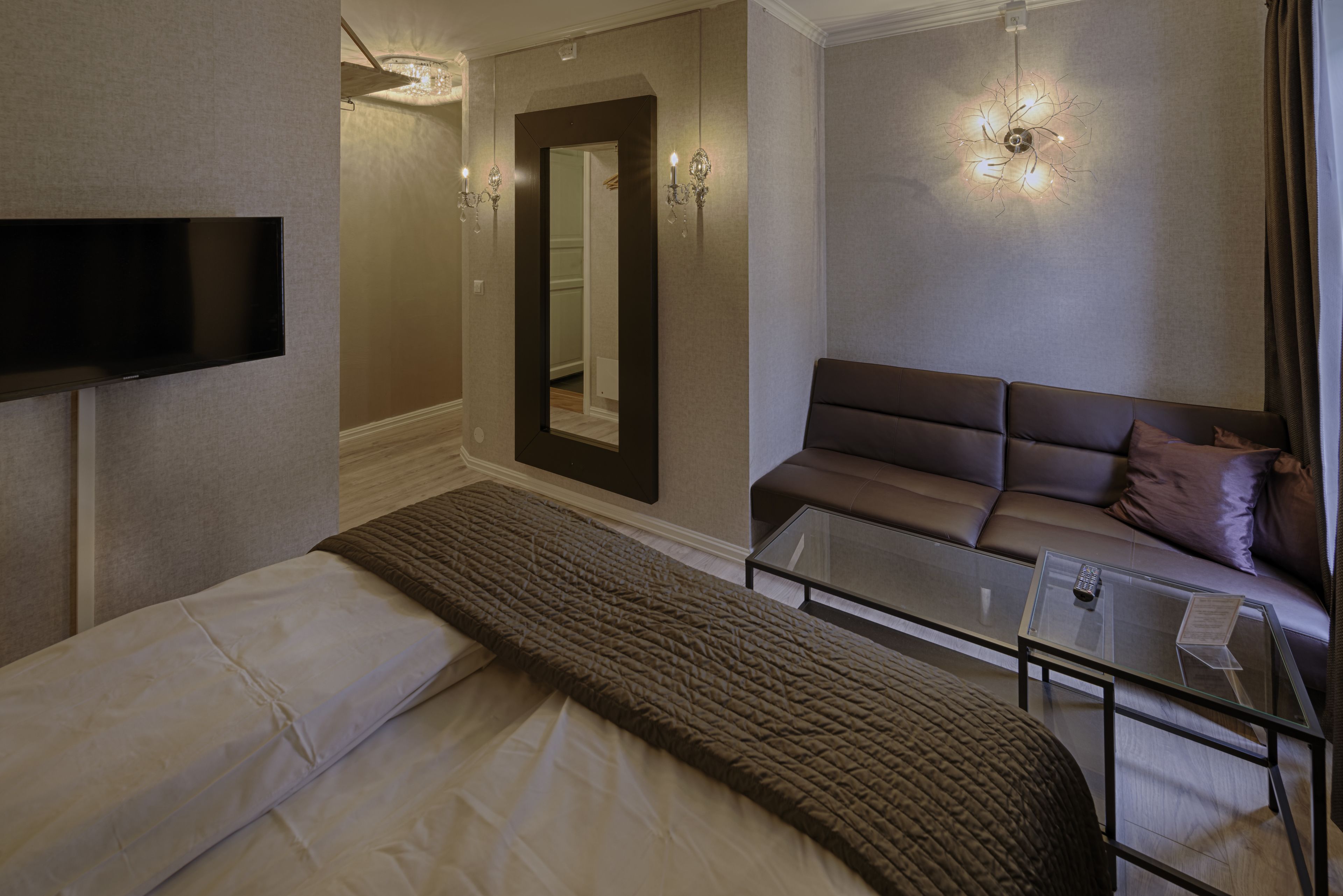 Ein Hotelzimmer mit Bett, Sofa, Glastisch, Flachbildfernseher an der Wand und Spiegel.